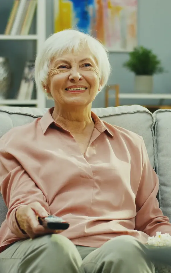 Eine Seniorin sitzt lächelnd auf dem Sofa.